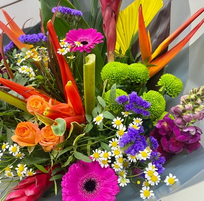 Vibrant Mother's Day bouquet featuring tropical flowers like ginger and heliconias alongside classic roses, germini, and daisy matricaria, wrapped in signature cellophane with a matching gift bag.