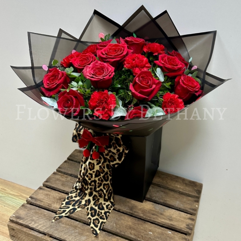 A new Valentine’s Day bouquet featuring red roses and carnations, wrapped in black cherry-print cellophane and topped with a detachable leopard print bow that doubles as a hair clip.