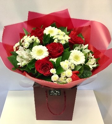 Bouquet featuring large luxury Freedom red roses, white germini, white chrysanthemums, red carnations, and white alstroemeria, accented with complementary foliage, wrapped in luxury cellophane and matching gift bag, hand-tied in water.