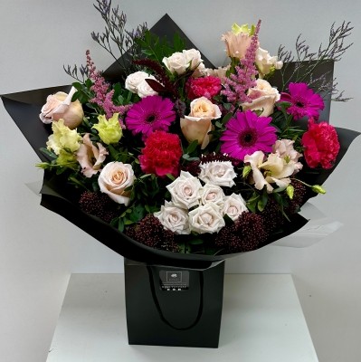 A beautiful bouquet containing roses, spray roses, germini, lizianthus, carnations, limonium, astilbe and skimmia in rich pink and nude tones, presented in a black gift bag and wrap. 