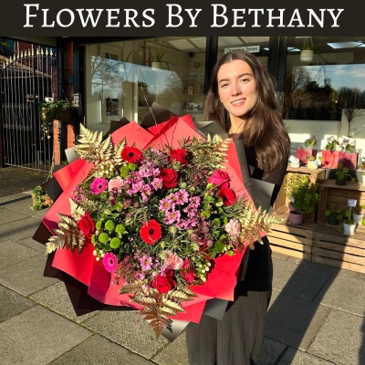 A luxurious bouquet featuring red roses, pink germini, green chrysanthemums, and gold-leaf accents among other seasonal florals. Wrapped in bold red and black wrapping with matching ribbon trails. 