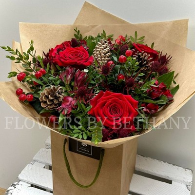 Mixed red bouquet including roses, alstroemeria, hypericum and thistle. Wrapped in kraft paper and displayed in a kraft bag. 