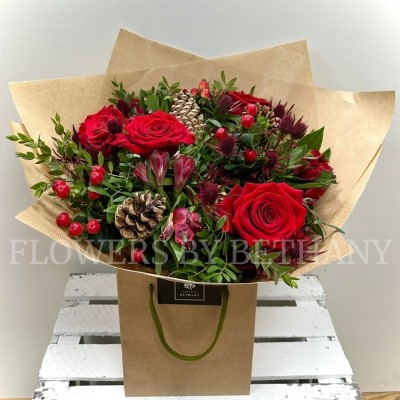 Mixed red bouquet including roses, alstroemeria, hypericum and thistle. Wrapped in kraft paper and displayed in a kraft bag. 