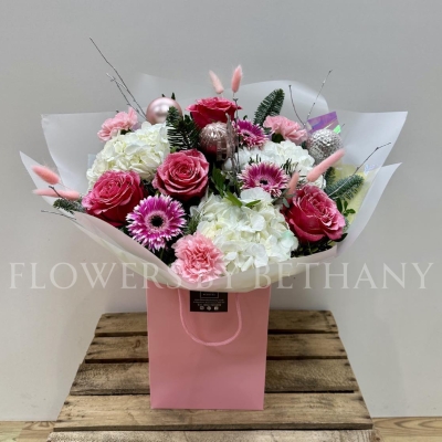 Snow Fairy Christmas bouquet featuring white hydrangea, pink snowy glitter roses, silver birch branches, mixed seasonal pink florals, pink baubles, and iridescent wrap, presented in a matching gift bag.