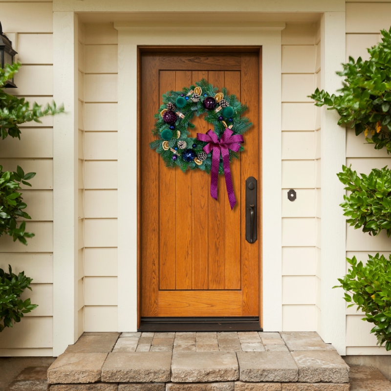 Fresh foliage door wreath with jewel toned accent baubles, dried orange slices, pine cones and cinnamon all brought together with a plush burgundy bow. 