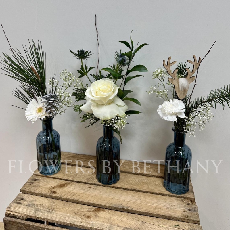 A gorgeous trio of deep blue bottles, each filled with festive foliage, crisp white florals and silver accent décor. The perfect item to dress your home or gift this Christmas. 