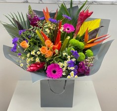 Vibrant Mother's Day bouquet featuring tropical flowers like ginger and heliconias alongside classic roses, germini, and daisy matricaria, wrapped in signature cellophane with a matching gift bag.