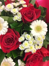 Bouquet featuring large luxury Freedom red roses, white germini, white chrysanthemums, red carnations, and white alstroemeria, accented with complementary foliage, wrapped in luxury cellophane and matching gift bag, hand-tied in water.