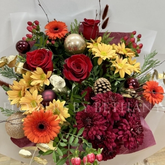 Fiery Festivities bouquet featuring orange germini, red chrysanthemums, red hypericum, red roses, pine cones, and gold baubles, presented in a burnt orange gift box with Christmas bow detailing