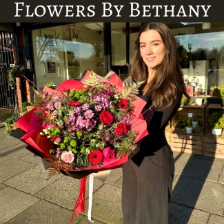 A luxurious bouquet featuring red roses, pink germini, green chrysanthemums, and gold-leaf accents among other seasonal florals. Wrapped in bold red and black wrapping with matching ribbon trails. 