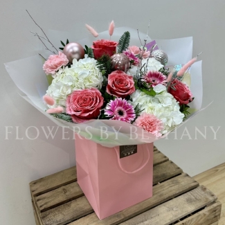 Snow Fairy Christmas bouquet featuring white hydrangea, pink snowy glitter roses, silver birch branches, mixed seasonal pink florals, pink baubles, and iridescent wrap, presented in a matching gift bag.